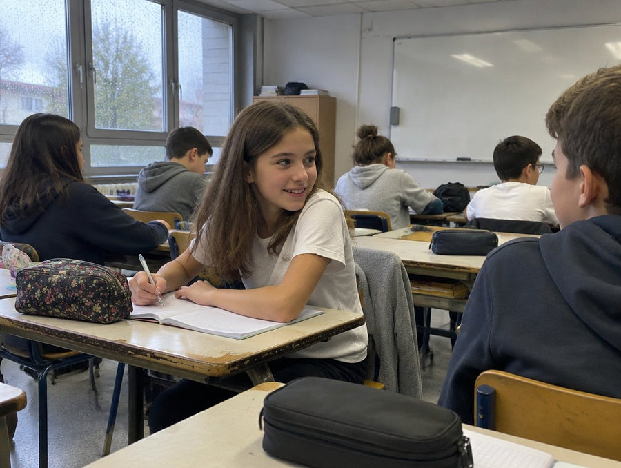 En classe, une fille en t-shirt clair écrit, son pull sur la chaise