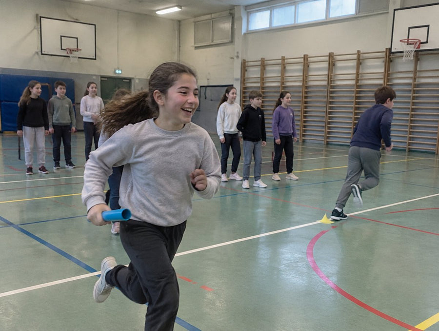 En EPS au gymnase, une fille court en riant pendant un relais